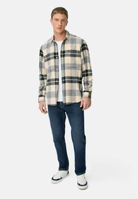 Geknoopte flanellen overhemd in crèmekleurige, grijze en zwarte ruit, gecombineerd met donkerblauwe jeans en witte sneakers. Lange mouwen met zakken.