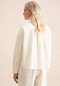 Cremefarbenes Hemd, lockere Passform mit abgerundetem Saum, mit Knopfmanschetten und weicher Textur. Verfügt über einen Kragen und minimale Details.