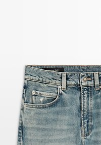 Hellblaue Jeans aus Denim mit Vordertaschen, Gürtelschlaufen, Knopfverschluss und einem sichtbaren schwarzen Markenlabel im Bundinnenseite.