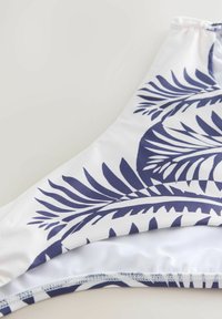 Fehér bikini alsó tengerészkék trópusi levélmintával és elasztikus derékpánttal, laposan elhelyezve világos felületen.