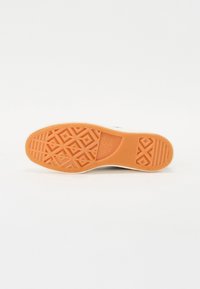 Suela de zapatilla blanca con una suela de goma naranja que presenta patrones de huella en forma de diamante y geométricos. Textura suave con acentos en relieve.