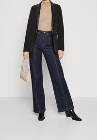 Černý blazer s saténovými klopami, béžový pletený svetr, tmavé džíny s vysokým pasem a širokými nohavicemi, černé boty na podpatku, béžová kabelka.