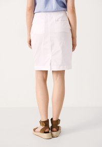 Jupe en coton blanche arrivant au genou avec deux poches arrière, présentant un détail fente en bas. Associée à des sandales espadrilles marron.