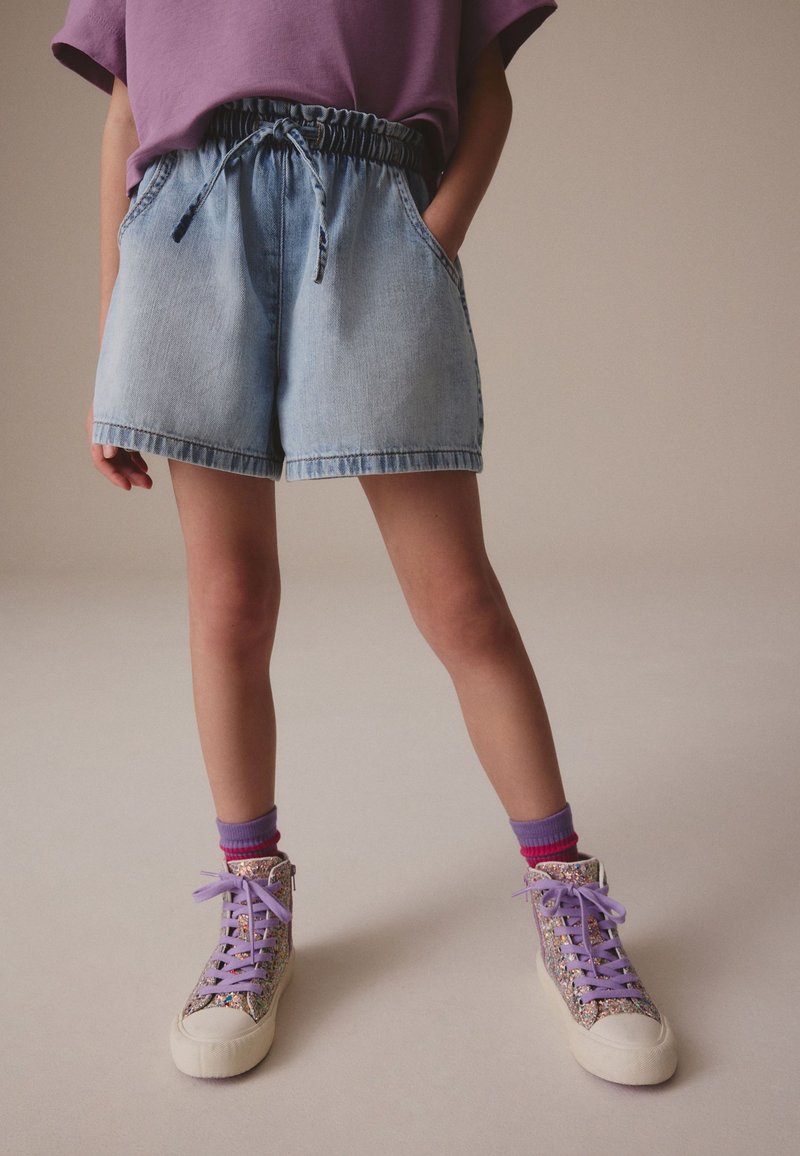 Jeansshorts mit elastischem Bund und Kordelzug in Hellblau, kombiniert mit schimmernden High-Top-Sneakern und mehrschichtigen, bunten Socken.