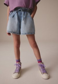 Denimshorts med elastisk talje og snøre, i lyseblå, kombineret med høje, skinnende sneakers og lag-på-lag farverige sokker.