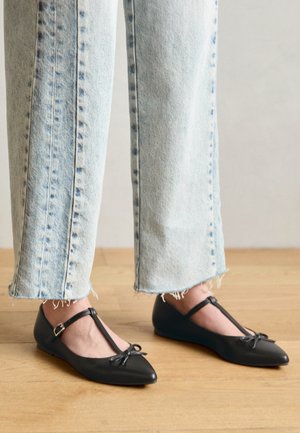 Zwarte T-strap ballerina's met een puntneus, strikdetail en verstelbare enkelband, gecombineerd met licht-gemaaide wijde jeans.