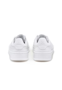 Un paio di sneakers platform in pelle bianca viste da dietro su uno sfondo bianco uniforme.