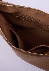 Ruskea nahkainen käsilaukku avattuna, näyttää sisävuoren kankaan, jossa on vetoketjullinen tasku ja useita lokeroita, kultaiset vetoketjukannat näkyvät.