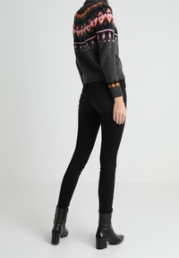 Šedý svetr s barevným geometrickým vzorem na výstřihu, spárovaný s černými skinny džíny a černými kotníkovými botami.