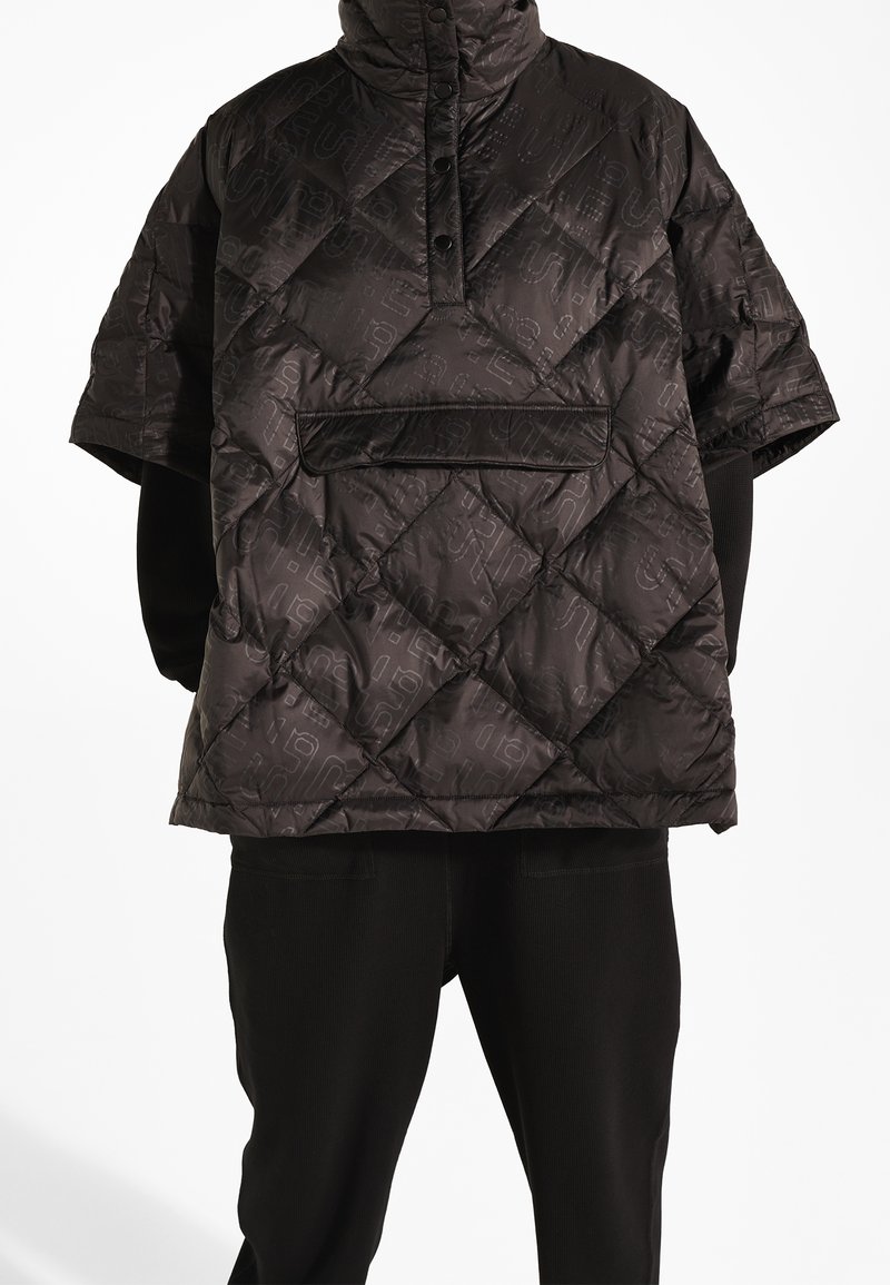 Veste courte matelassée noire avec couture en losanges, boutons-pression à l'avant et poche à rabat, portée sur un haut noir à manches longues et un pantalon.