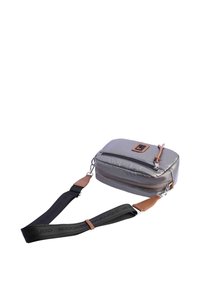 Bolsa de nailon gris con forma rectangular, cierre de cremallera, detalles en cuero marrón y una correa ajustable negra. Presenta una superficie texturizada.