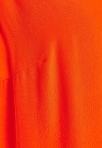 Ljus orange tyg med en texturerad, något skrynklig yta; har en söm på ena sidan med en slät finish.