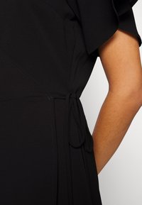Black dress with short, ruffled sleeves, a defined waistline, and a side tie detail. Smooth texture with subtle stitching accents.