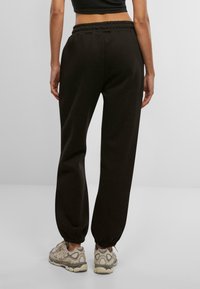 Pantalons de survêtement noirs avec une taille élastique et des poignets, présentant une texture lisse. Accentué par une coupe décontractée, associé à des baskets beiges.