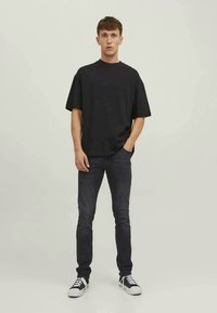 T-shirt nera in cotone con maniche corte, vestibilità rilassata. Abbinata a jeans scuri e sneaker nere. Design semplice, senza modelli o accenti visibili.