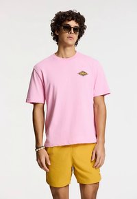 Pink cotton t-shirt with short sleeves and a diamond-shaped yellow graphic on the chest, paired with yellow shorts.
