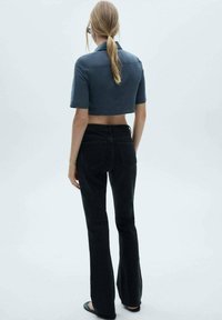 Gekürztes navyblaues Kurzarmhemd kombiniert mit hochgeschnittenen schwarzen Schlagjeans, die ein figurschmeichelndes Design und glatte Texturen aufweisen.