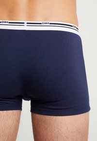 Tmavě modré bavlněné boxerky s bílým páskem se značkou a dvěma černými pruhy, hladká textura a přiléhavý střih.