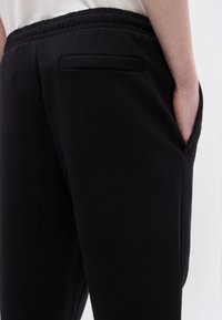 Μαύρη φόρμα από απαλό ύφασμα, με ριμπ ζώνη μέσης, πλαϊνές τσέπες και μια πίσω τσέπη με κομψό σχέδιο.