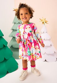 Vestido rosa colorido con mangas largas, con estampados festivos de Santa, muñecos de nieve y adornos. Combinado con zapatillas blancas y calcetines rosas.