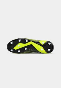 Sola de chuteira de futebol preta e amarela com superfície texturizada, apresenta seis cravos brancos e um design em zigue-zague para tração.
