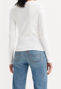 Vit långärmad topp i kombination med blå denimjeans, med en avslappnad passform och en subtil textur på båda plaggen.