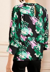 Blusa nera con vivaci motivi floreali verdi, rosa e bianchi. Tessuto morbido, maniche a sbuffo e dettaglio di chiusura a fessura sulla schiena.