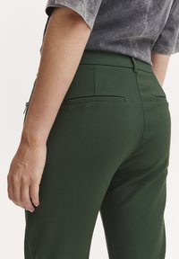 Grønne skræddersyede bukser lavet af glat stof, med en middels høj talje, to baglommer og et rent, tætsiddende design.