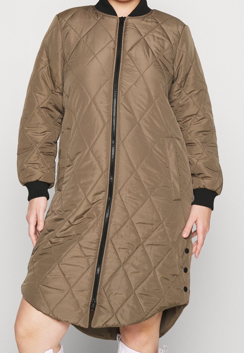 Chaqueta bomber larga acolchada de color verde oliva con puños y cuello de canalé negros, cremallera frontal, bolsillos laterales y botones de presión en el lado de la parte inferior.