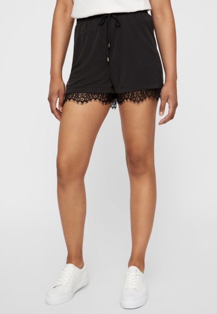 Shorts noirs en tissu doux avec une taille à cordon, bord en dentelle à l'ourlet et une coupe décontractée, associés à des baskets blanches.