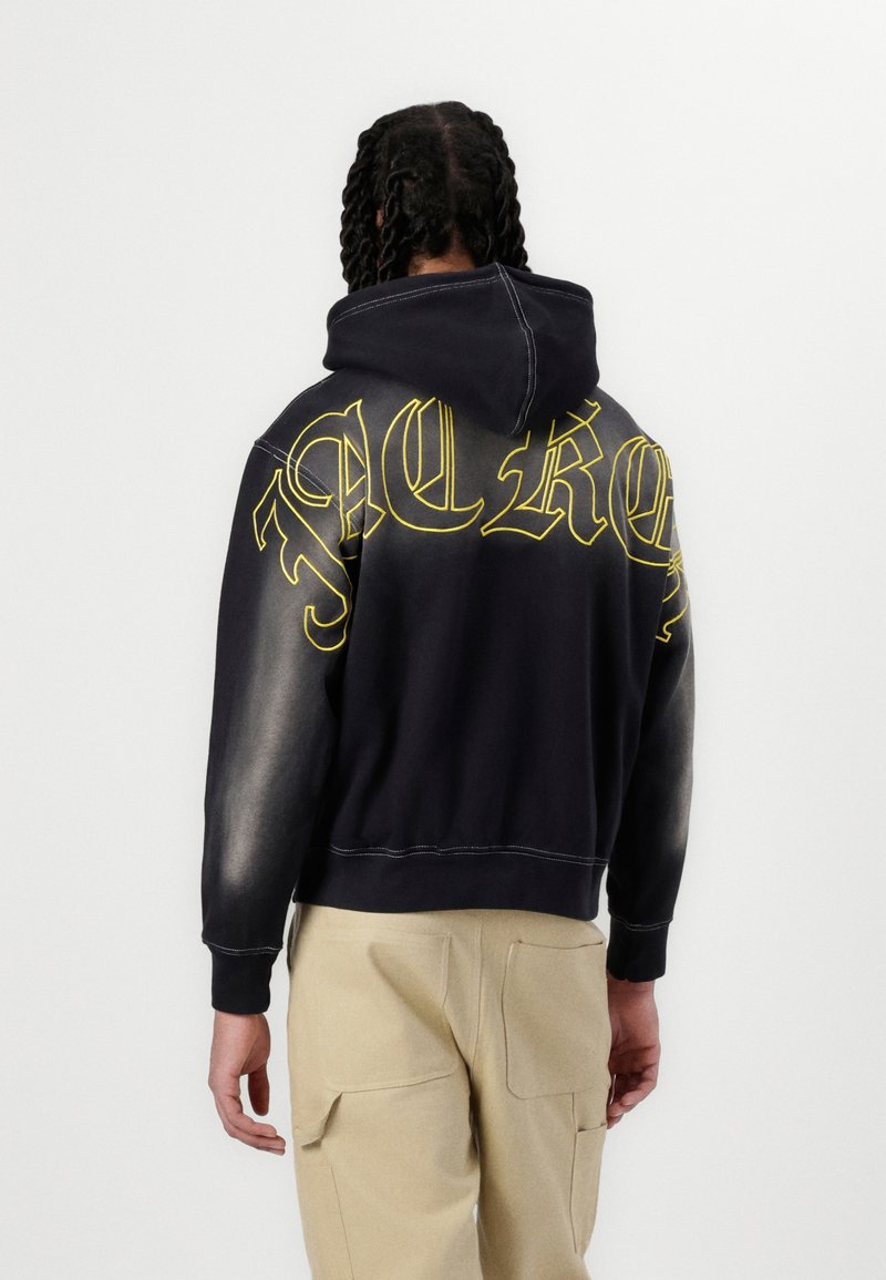 Moleton preto com letras amarelas nas costas, apresentando um design encurtado e mangas mais claras em contraste. Tecido macio com costuras visíveis.