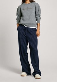 Sudadera gris con un logo texturizado en la parte delantera, combinada con pantalones de pierna ancha a rayas navy y zapatillas blancas.