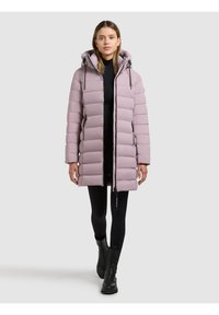 Lichtroze gewatteerde jas met capuchon, voorzien van een verticale doorgestikte structuur, zijritsen en een getailleerde taille, gecombineerd met zwarte leggings en laarzen.