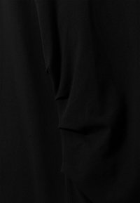 Sort stof med en blød tekstur, der har en draperet silhuet og delikate folder, hvilket skaber et lagdelt udseende.