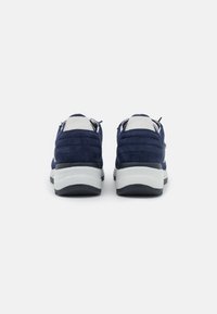 Navy suede kengät valkoisella kumipohjalla. Varustettu pehmustetulla kauluksella ja nauhoitusjärjestelmällä. Siisti muotoilu, jossa on teksturoitu päällinen.