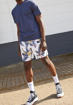 Granatowy bawełniany t-shirt w połączeniu z białymi szortami z kolorowym wzorem kwiatów i ptaków, dopełniony czarnymi trampkami typu high-top i białymi skarpetkami.