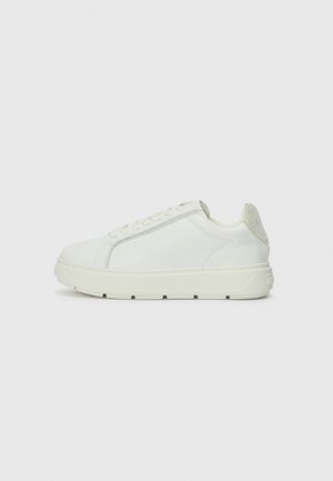 White sneaker with a smooth finish, round toe, and textured heel tab. Features laces and a chunky sole with subtle tread pattern.