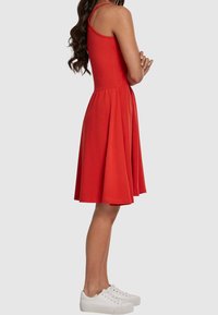 Robe sans manches rouge avec un corsage ajusté et une jupe évasée. Fabriquée en tissu doux. Assortie à des baskets blanches.