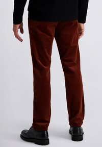 Brown corduroy pants with vertical ribbing, featuring a relaxed fit and worn with black leather shoes. Visible back pocket seams.