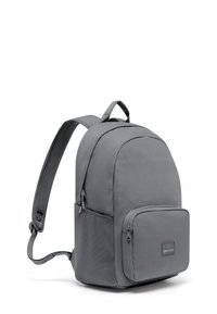 Grå tygryggsäck med rundad form, framficka med dragkedja, justerbara remmar och ett handtag högst upp. Slät textur med subtila sömnadsdetaljer.