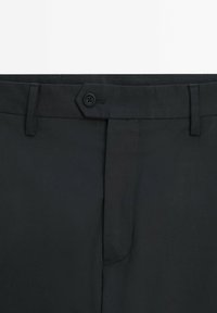 Pantalon noir à texture lisse, avec un bouton hexagonal, une fermeture avant et des passants pour ceinture. Le tissu présente un motif subtil.
