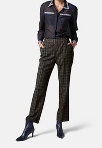 Transparante donkerblauwe blouse met versierde kraag en zakken; hooggerokte ruitenbroek in donkere tinten; nauwsluitende marineblauwe enkellaarzen.