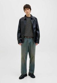 Sort læderjakke over en stribet sort og hvid sweater, parret med lyseblå, baggy jeans og sorte sko.
