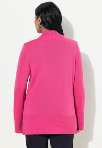 Pull en tricot rose avec un col montant, un ourlet côtelé et des manches longues. Présente des fentes sur les côtés et des boutons décoratifs sur les poignets.