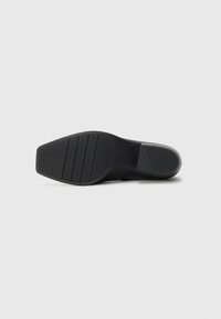 Soletta nera con motivi di grip testurizzati, caratterizzata da una punta arrotondata e un tacco leggermente sollevato. Realizzata in gomma e materiali sintetici.