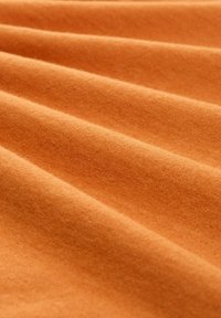 Oranges Baumwollstoff mit einer weichen Textur, der sanfte Falten und eine glatte, gleichmäßige Oberfläche aufweist.