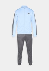 Φωτεινό γαλάζιο παντελόνι φόρμας με όρθιο γιακά και φερμουάρ, σε συνδυασμό με σκούρο γκρι παντελόνι· διαθέτει τρεις μαύρες ρίγες στα μανίκια και λογότυπο.