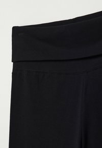 Musta legginsit, joissa on leveä vyötärönauha, valmistettu pehmeästä kankaasta. Muotoilu on sileä, ilman näkyviä saumoja tai kuvioita.