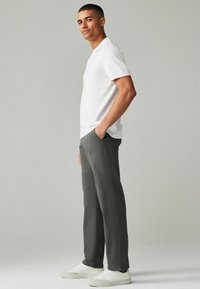 Polo bianco abbinato a pantaloni grigi, realizzati in tessuto leggero. Presenta un colletto classico, taglio dritto e linee pulite. Sneakers bianche.