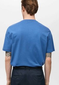 Tricou cu mânecă scurtă, guler rotund, din bumbac albastru solid, cu o croială relaxată și o textură uniformă, purtat cu pantaloni negri.